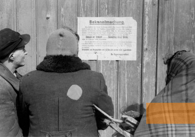 Image: Ciechanów, 1941, Jews in front of a notification (dated January 18, 1941) on the destruction of buildings in Ciechanów, PK 689, Ludwig Knobloch, Bundesarchiv, Bild 101I-133-0730-13