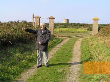 Image: Alderney, 2008, Survivor Sylwester Kukula in front of the former gate to Lager Sylt, Yolanta Boot