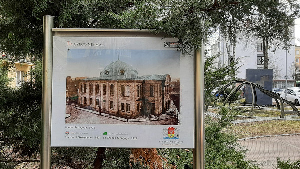 Bialystok, 2023, Tafel mit einem Bild der ehemaligen Synagoge mit dem Denkmal im Hintergrund, Stiftung Denkmal